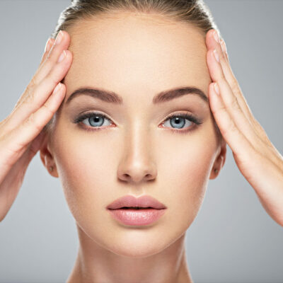 A woman with braces on her teeth covering her face in surprise.
